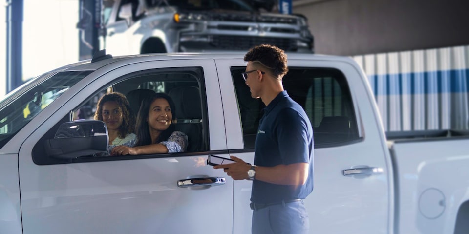 Duas mulheres dentro de um Chevrolet, sendo atendidas por um homem representando os Serviços Chevrolet